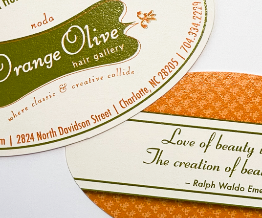A cropped close up of die cut oval-shaped business cards featuring the Orange Olive logo and contact information on the front, and a quote by Ralph Waldo Emerson on the back