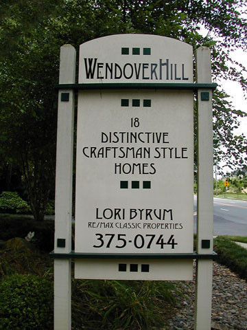 A wooden sign with beige paint and black writing that reads Wendover Hill, 18 distinctive craftsman style homes, and includes the name and number of a realor named Lori Byrum